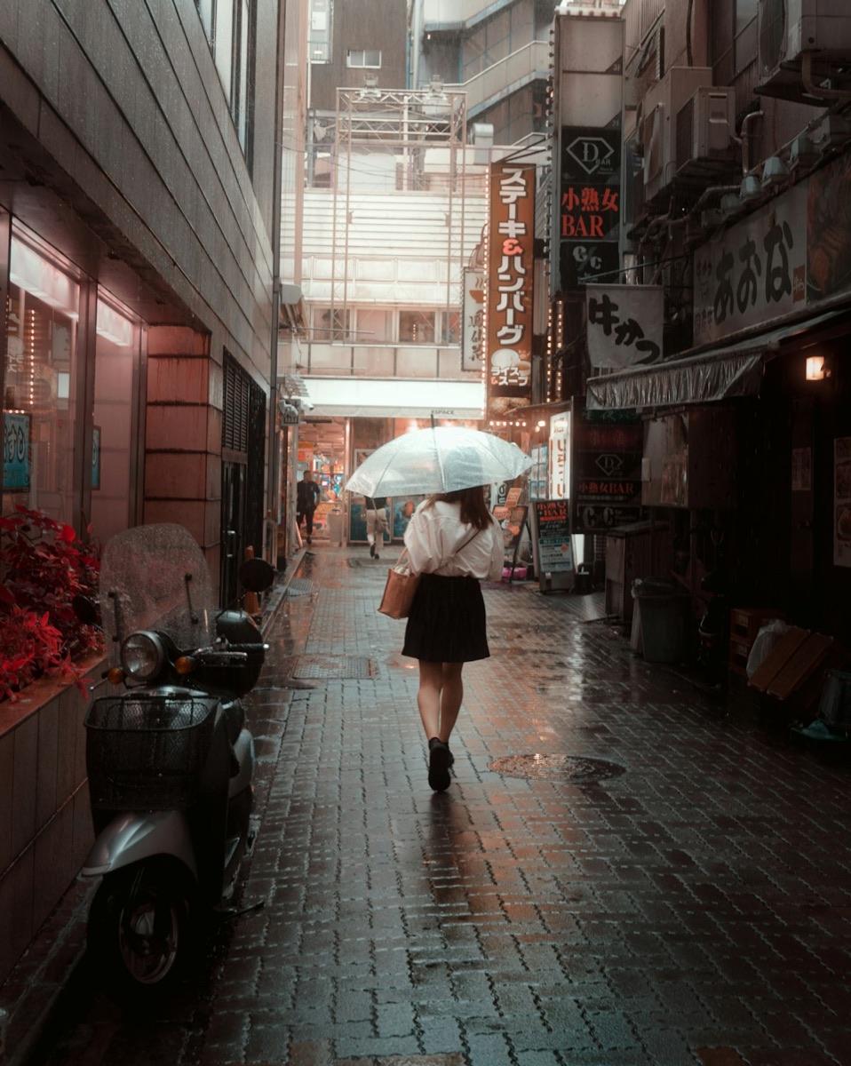 A woman in Tokyo walking with an umbrella down a city street during light rain