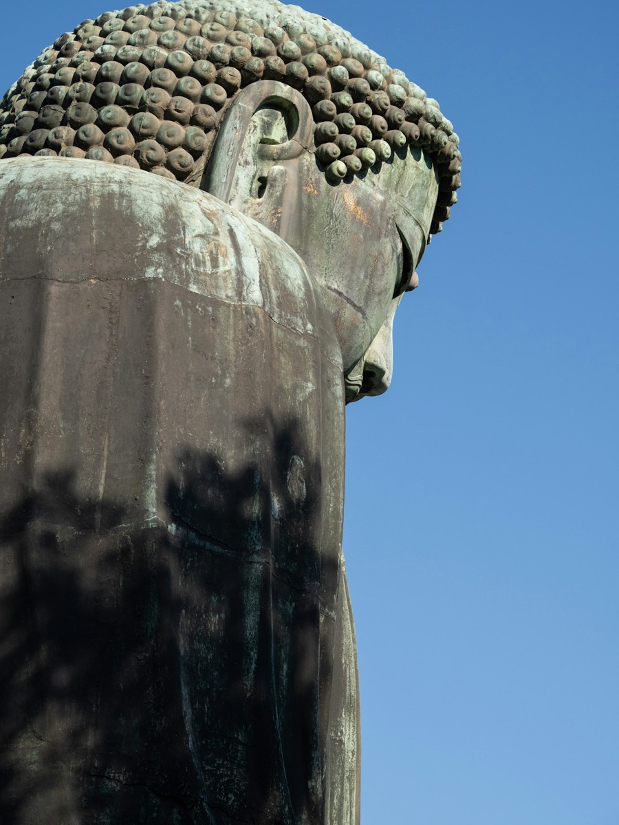 The Kamakura Great Buddha bronze statue against a blue sky with travelers visible at the base