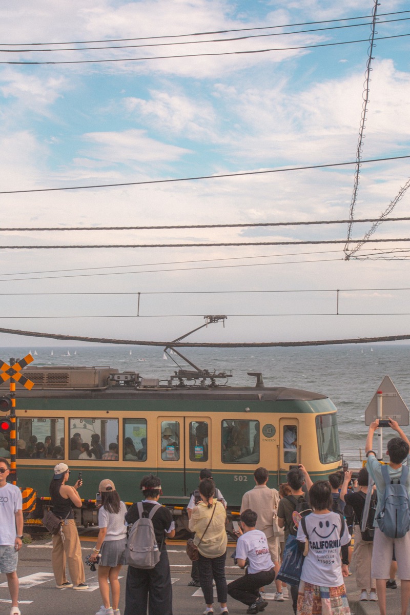 The Enoden train passing by the ocean in Kamakura with travelers watching