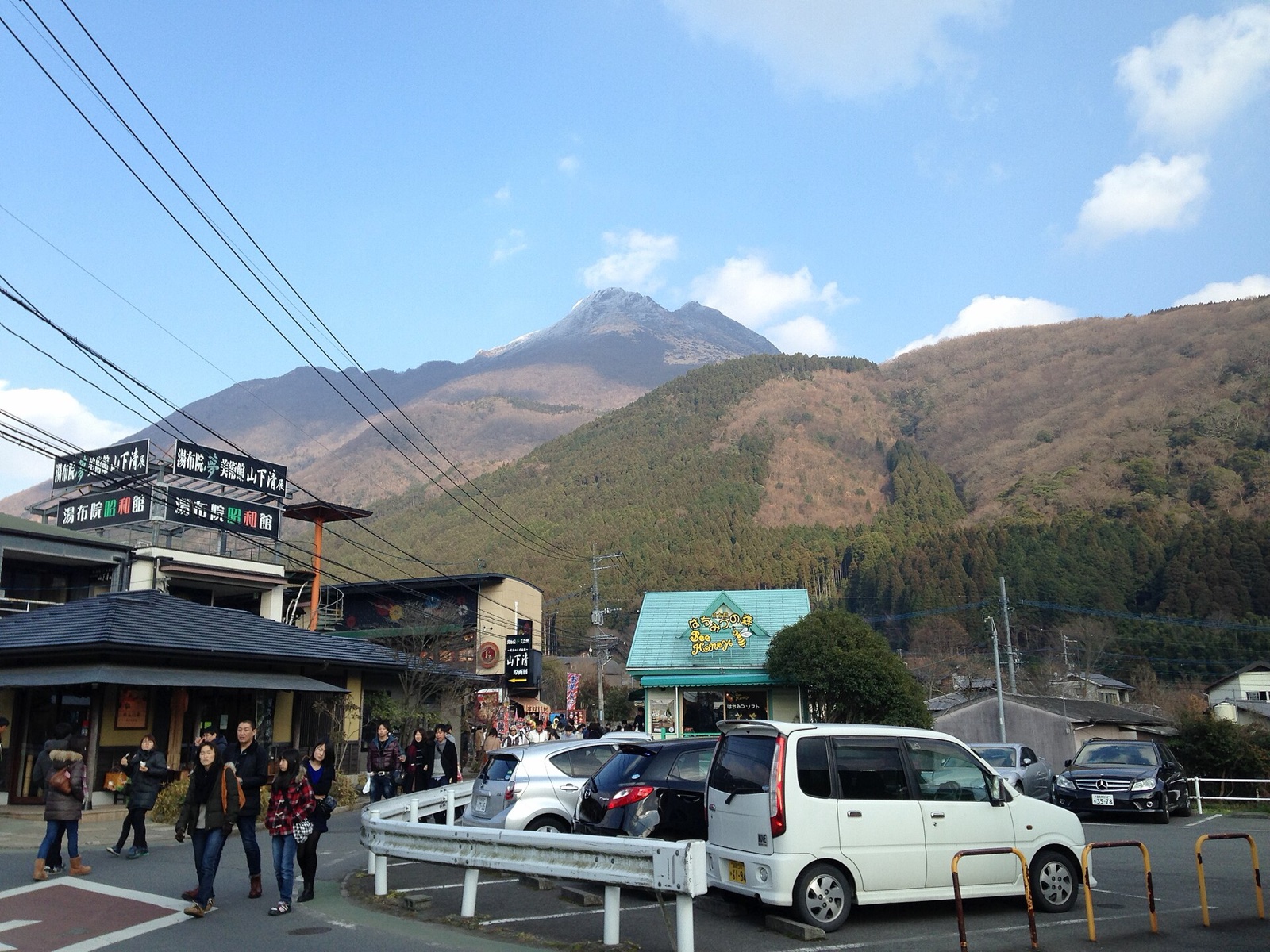 Mount Yufu rising behind shops, pedestrians and cars near Yunotsubo Street