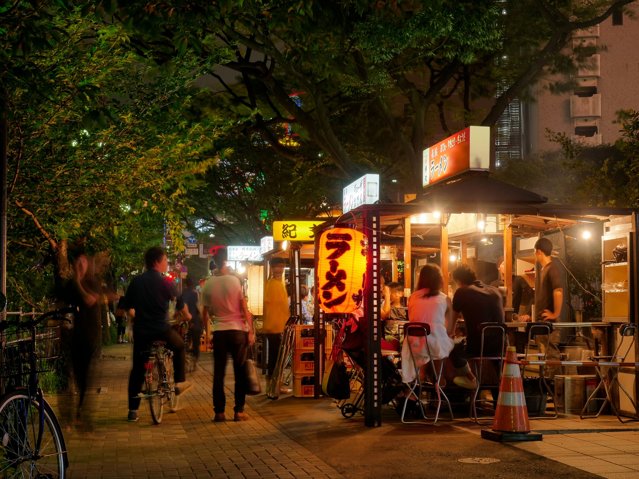 Customers eating at illuminated yatai food stalls under trees in Fukuoka