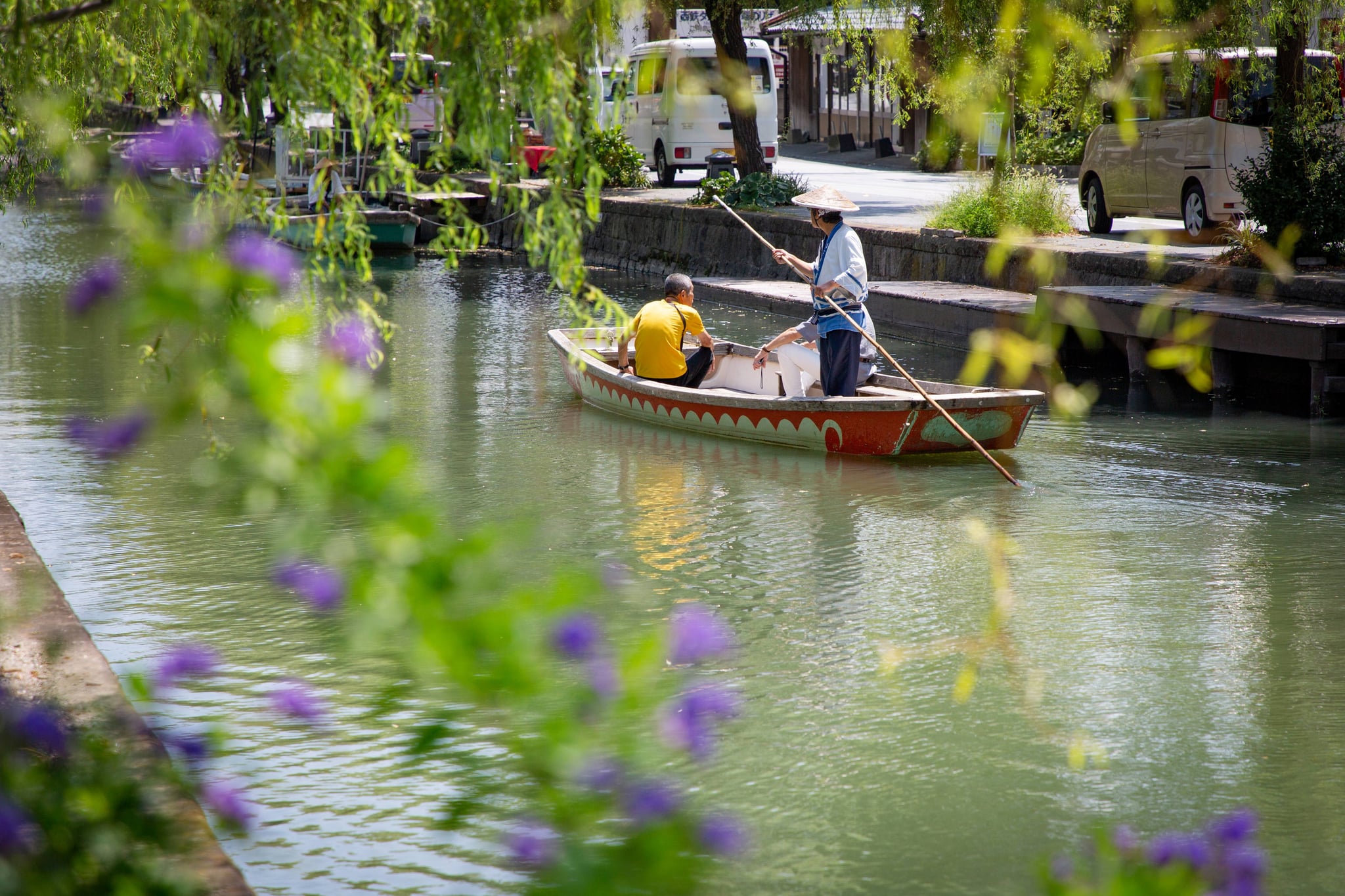 A boatman poling a sightseeing boat along a willow-lined canal in Yanagawa