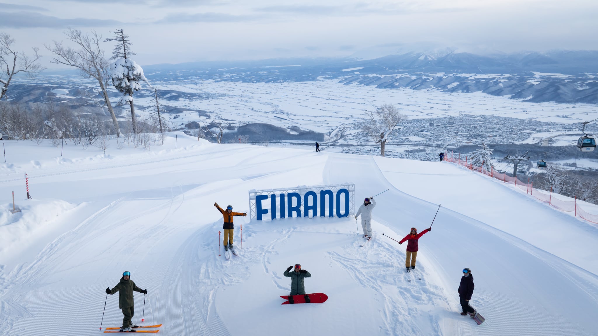 Skiers beside the FURANO sign with a broad snowy valley behind them