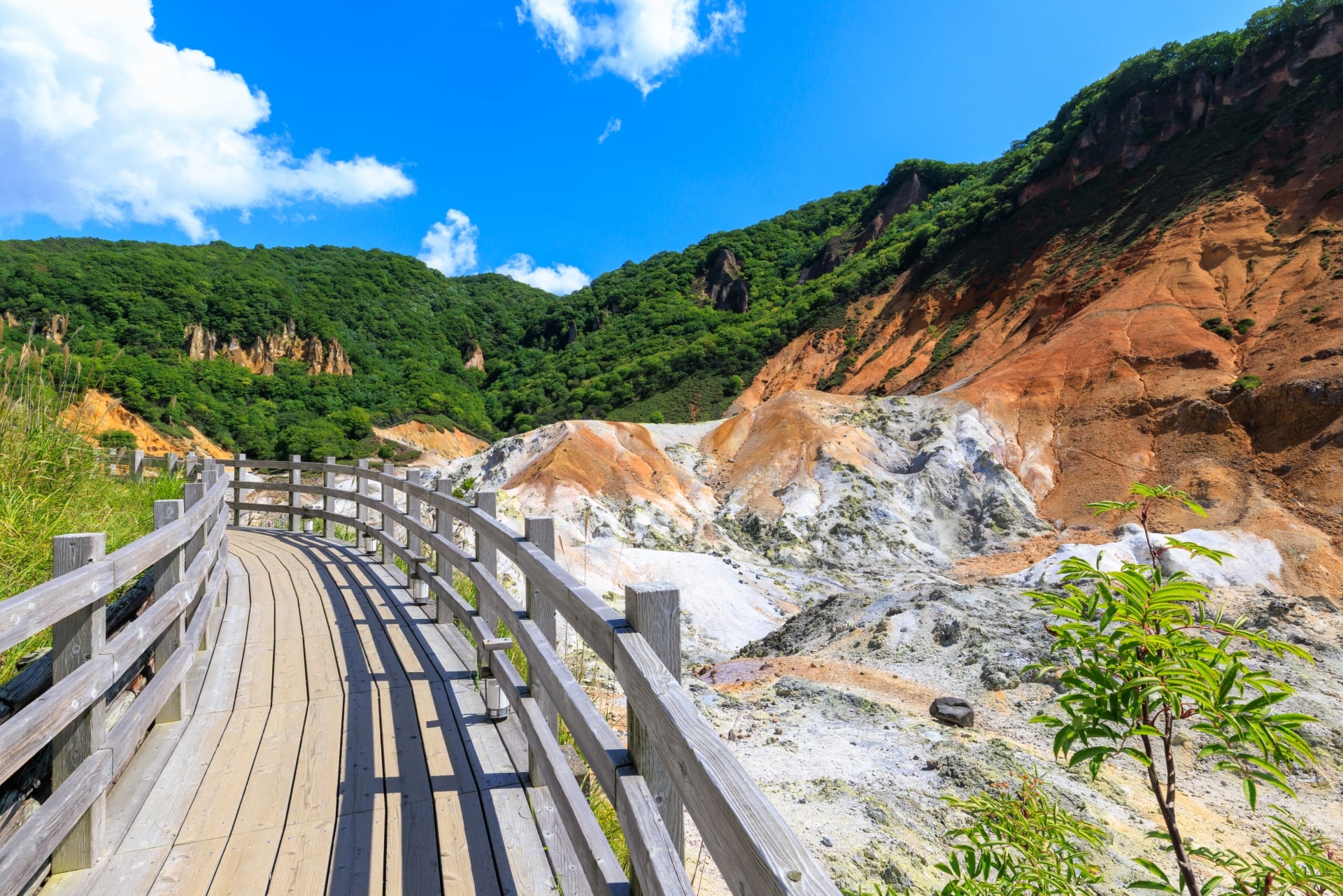 Wooden walkway passing pale mineral slopes and green hills at Noboribetsu Hell Valley