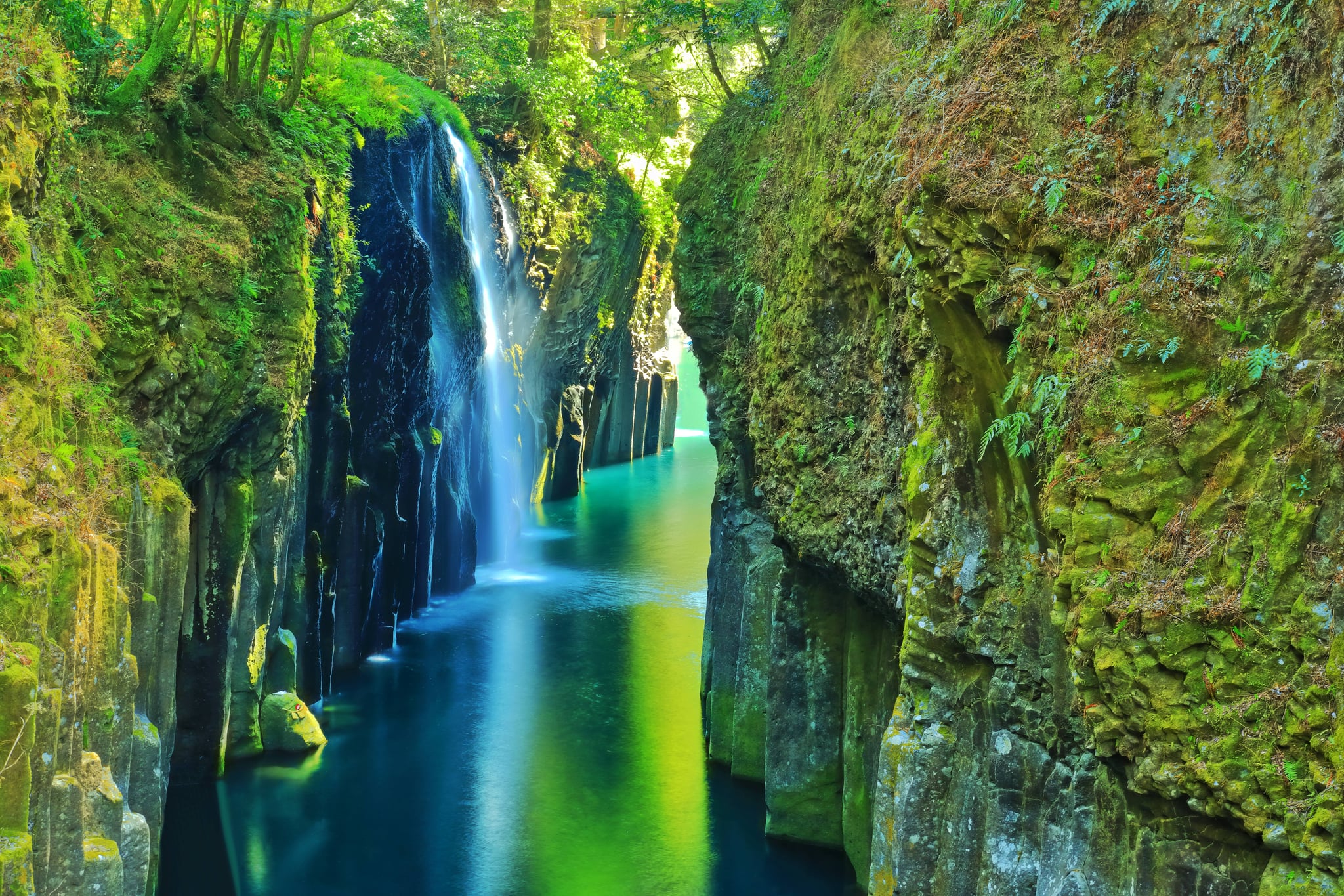 Waterfall dropping into Takachiho Gorge below steep rock walls and green trees