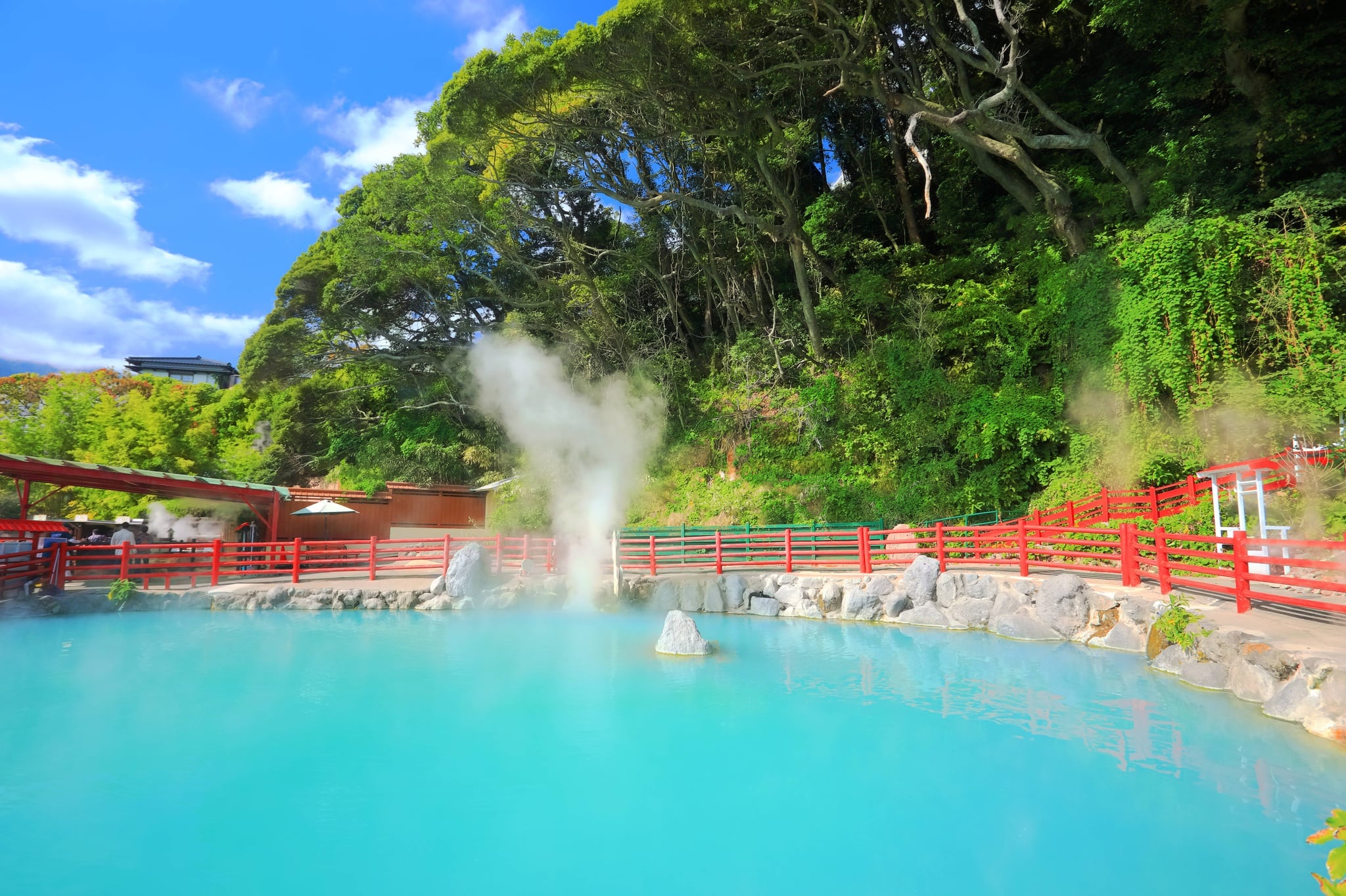 Steam rising from a turquoise geothermal sightseeing pool with red railings in Beppu