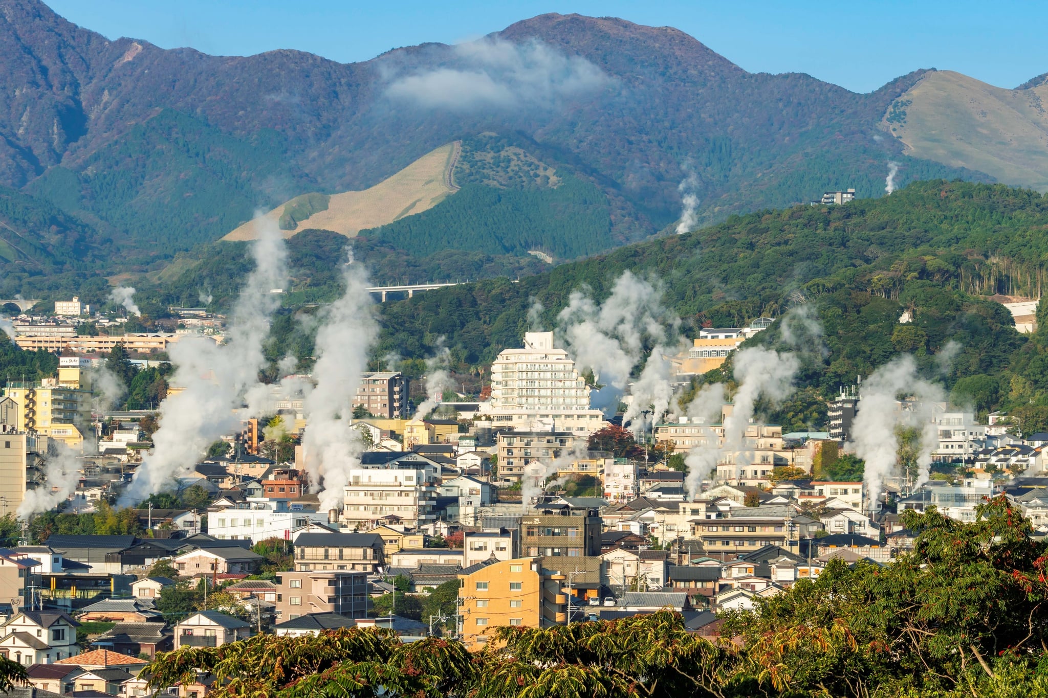 Steam rising from rooftops in Beppu with green hills behind the city